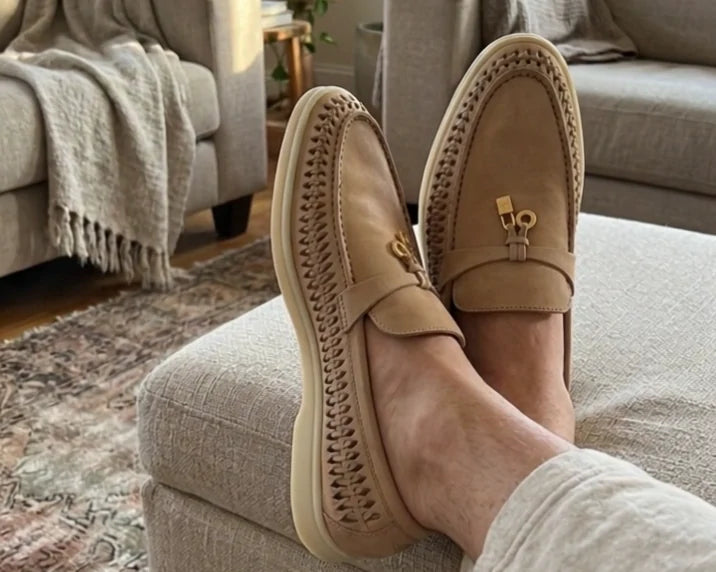 Sand loafers worn with relaxed trousers, feet resting on a fabric ottoman at home